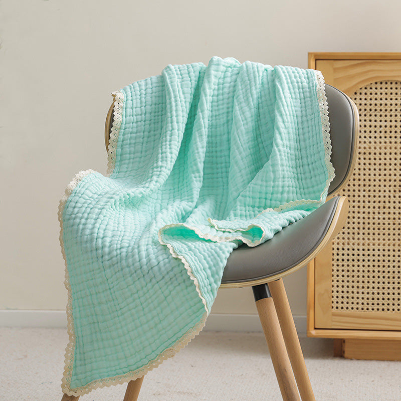 A soft mint green 6-layer cotton gauze baby blanket with intricate lace trim draped over a gray chair.
