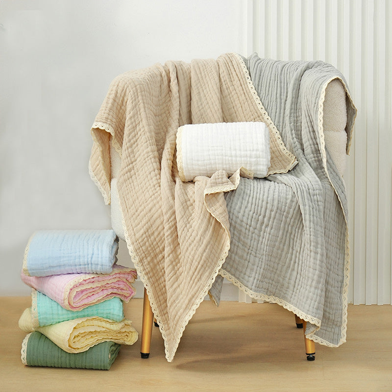 A stack of colorful 6-layer cotton gauze muslin baby blankets with lace trim, next to a chair holding two folded blankets in beige and gray.
