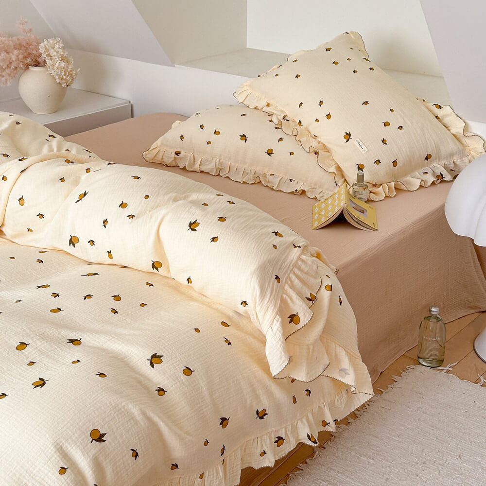 A view of a twin bed with the Zesty Lemon cotton muslin duvet set. The image shows the bedding's light yellow color, the playful lemon pattern, and the ruffled trim