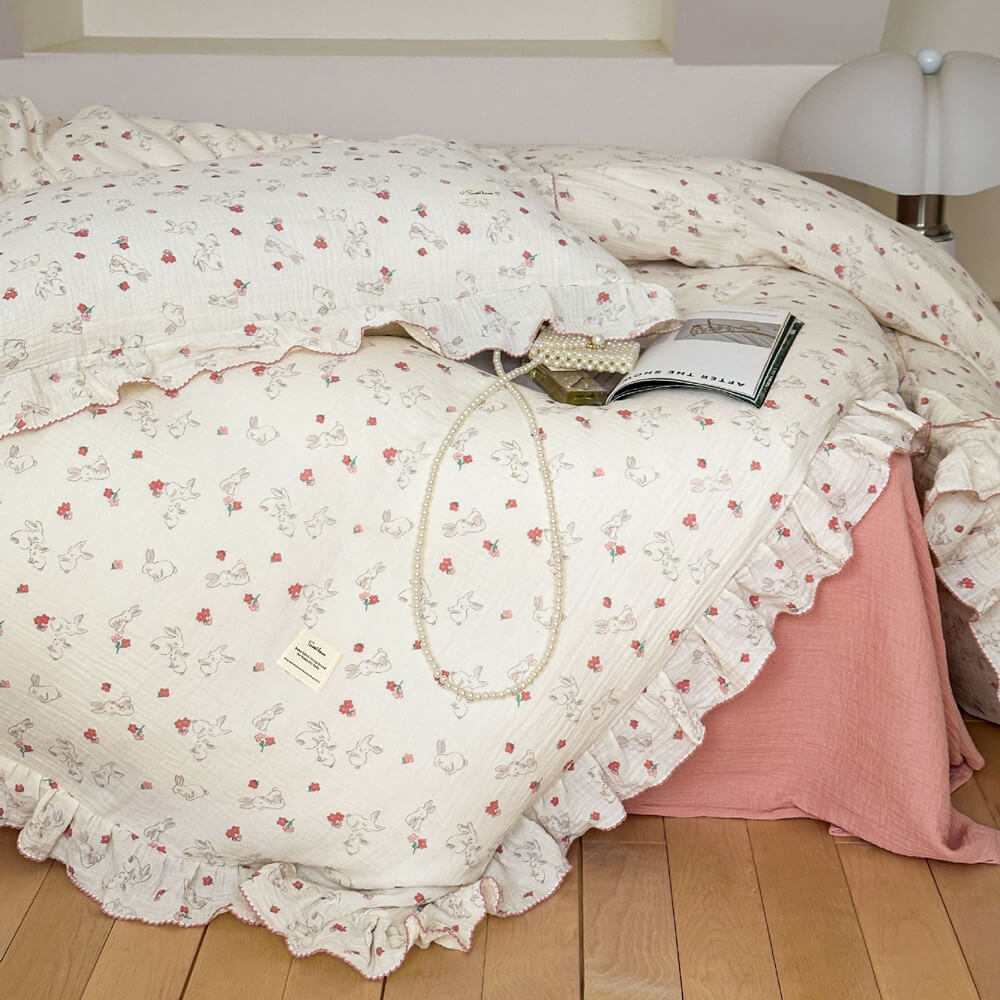 A close-up view of a bed with a white duvet cover set, showcasing the adorable bunny and red floral pattern on soft cotton muslin with ruffled trim.