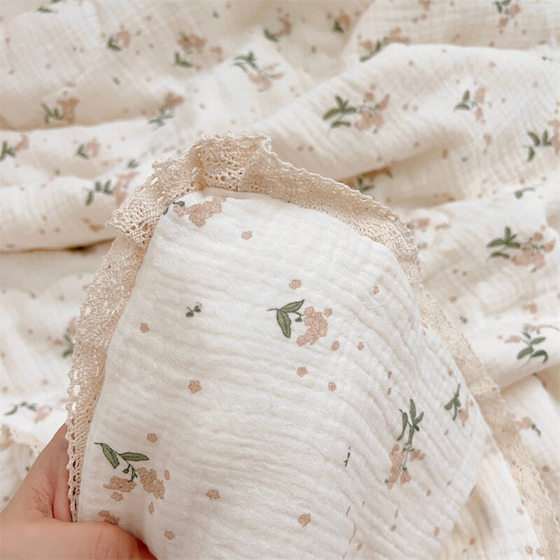 Lace-trimmed corner of a floral cotton muslin baby blanket in cream and green tones