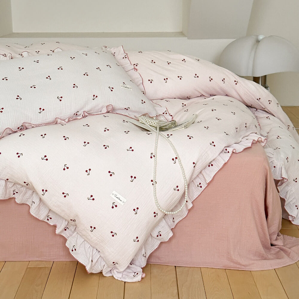 A bed styled with the pink cherry print cotton muslin duvet cover set, featuring ruffle edges and a decorative pearl necklace.