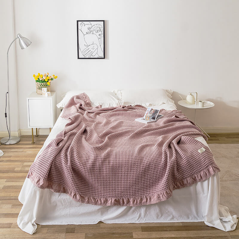 blush pink cotton waffle blanket with ruffle edge displayed on a bed