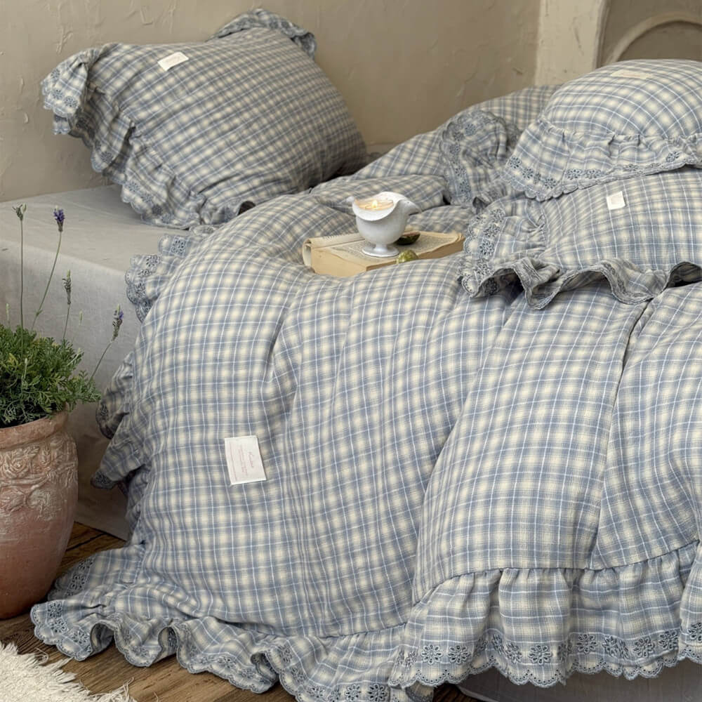 Bedside view of dusty blue plaid ruffle bedding, lace trim and wooden nightstand
