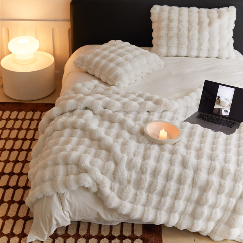 Fluffy off-white faux rabbit fur throw blanket styled on a bed with matching pillows.