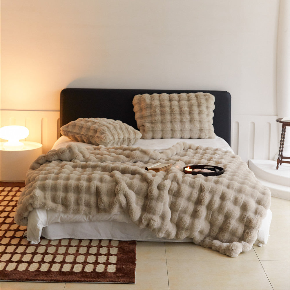 Fluffy khaki faux rabbit fur blanket and pillows on a bed, showcasing the cozy texture.