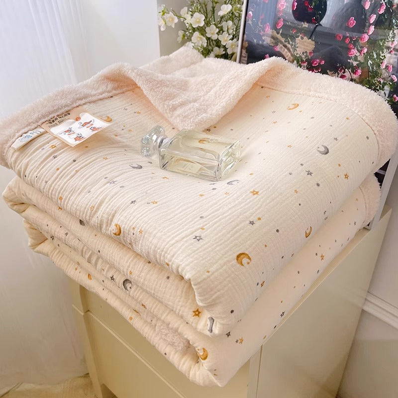 A reversible fleece throw blanket with a moon and stars pattern, folded on a cabinet, offering warmth and a celestial design.