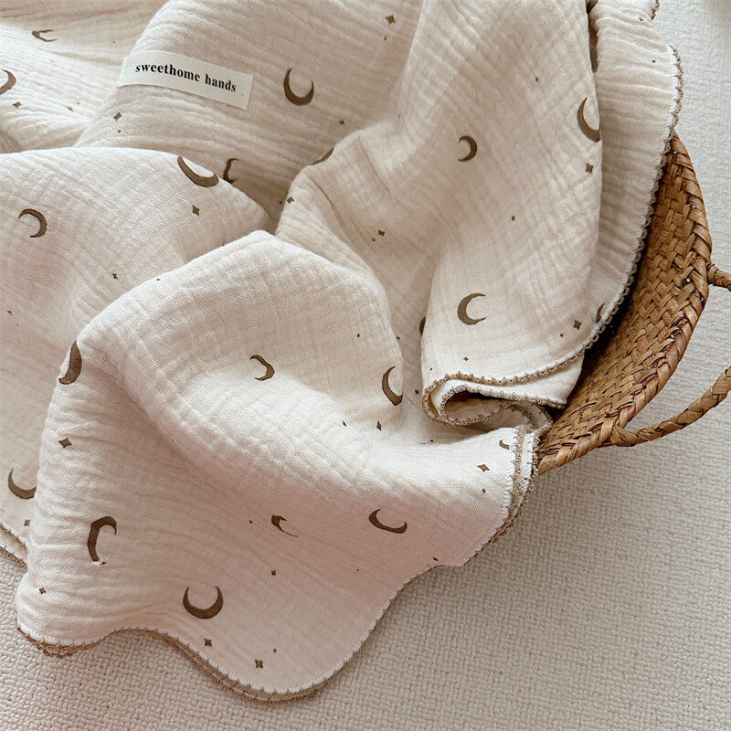 Close-up of a lightweight brown moon and star muslin baby blanket with decorative scalloped edges, suitable for boys and girls.