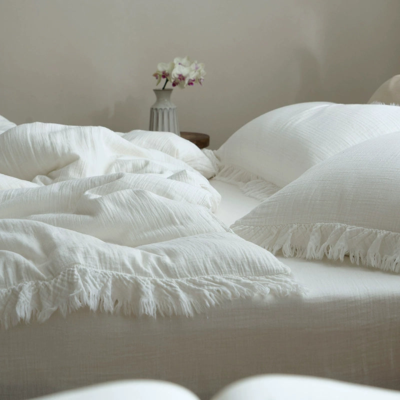 A view of the white cotton gauze bedding set with fringe, showing the duvet cover and pillows on a bed with a vase of flowers in the background, creating a serene atmosphere