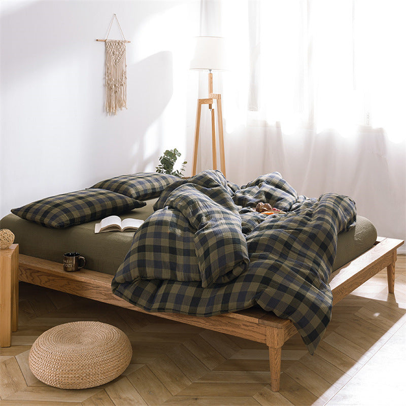 A cozy bed setup featuring army green and navy plaid bedding, with a ruffled comforter and matching pillows in a sunlit room.