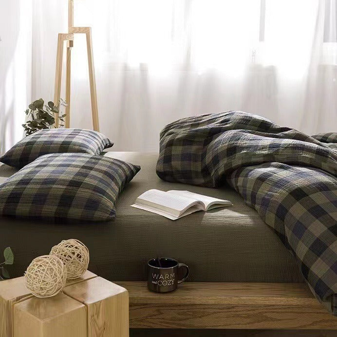 Front-facing shot of a bed covered in checkered army green bedding, styled with decorative plants and wooden furniture in a minimal bedroom.