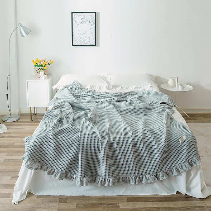 light grey cotton waffle blanket with ruffle edge displayed on a bed