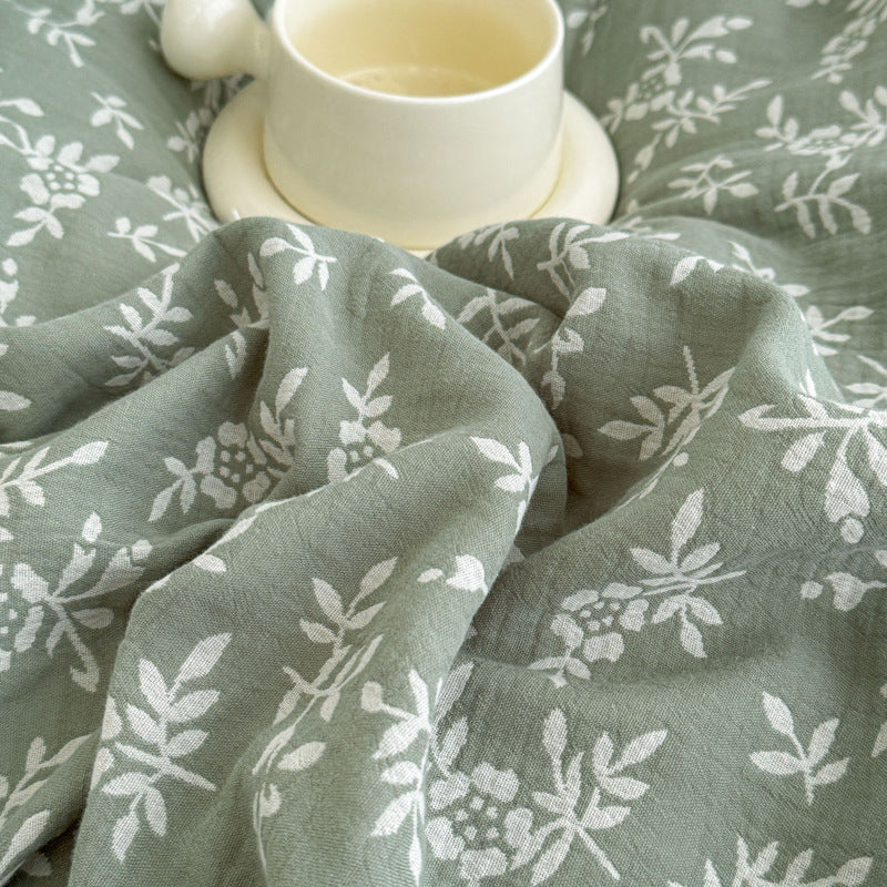 A close-up shot of the green jacquard cotton duvet cover with a white woven leaf pattern and a cup of coffee resting on it.
