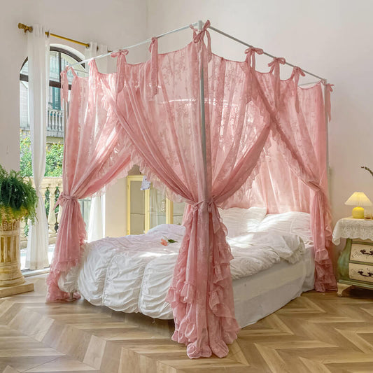 A charming pink floral lace bed canopy with ruffle trim, tied back to show a bright bedroom with a white 4-poster bed and white bedding.