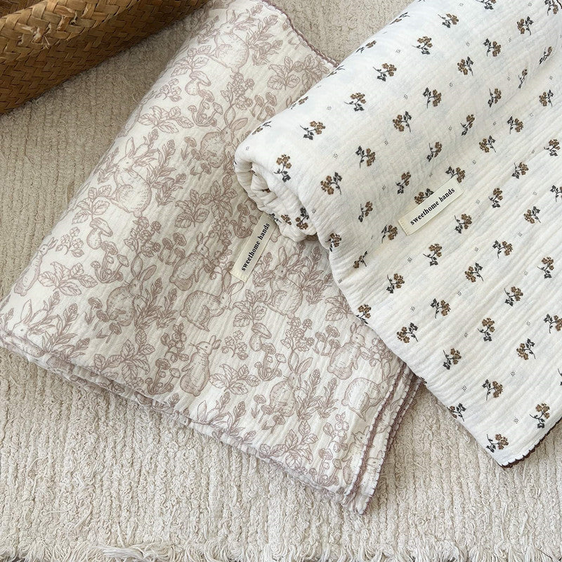 A set of two soft, large muslin baby blankets: one with a Dreamwoods floral rabbit pattern and one with a simple floral pattern.