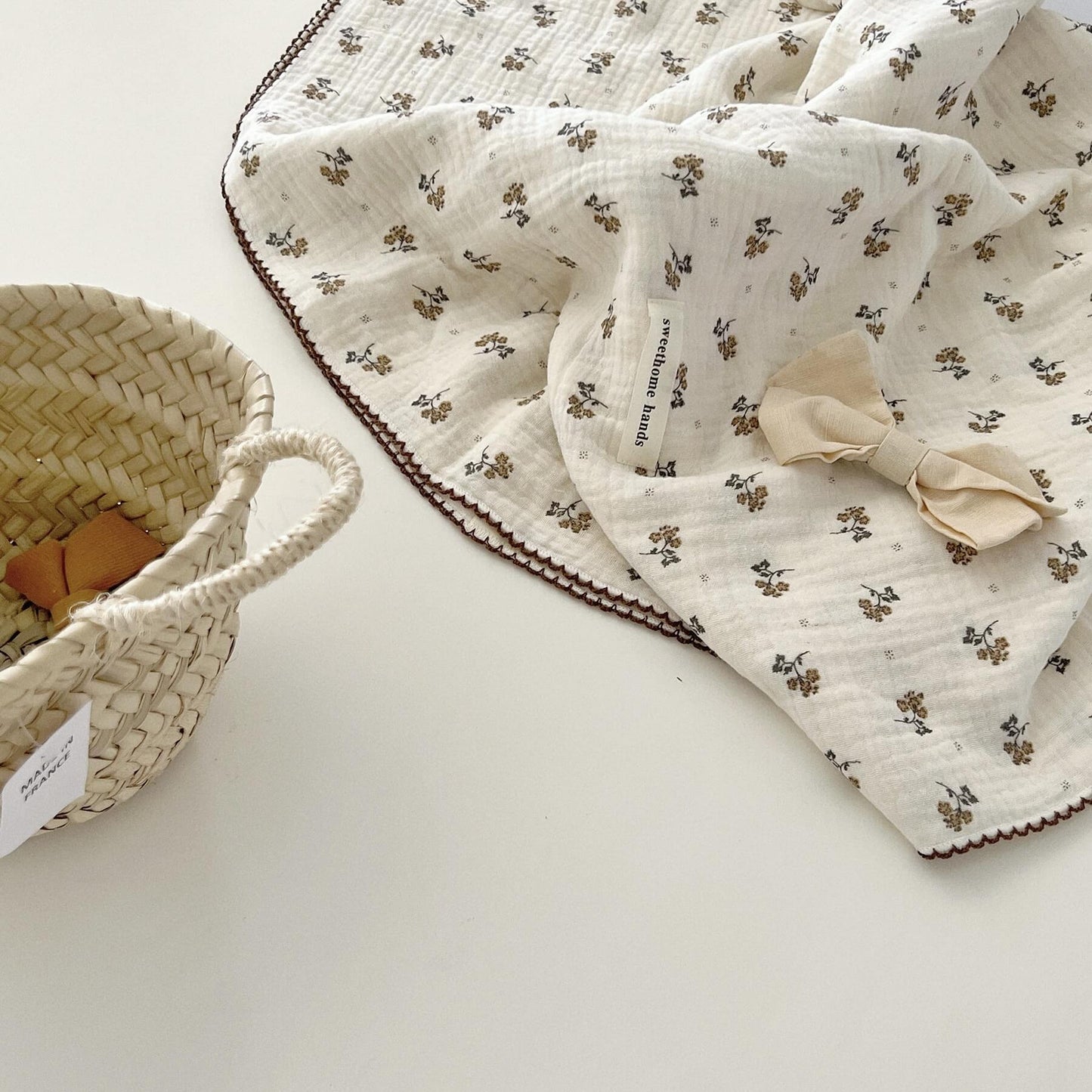 A tightly rolled-up Calendula Floral muslin toddler blanket placed inside a woven wicker basket, perfect for travel or storage.
