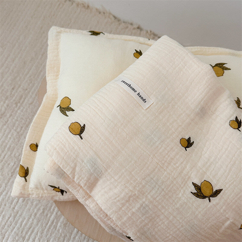 A close-up of a soft muslin cotton baby blanket with a pillow set, featuring a cheerful lemon print fabric texture