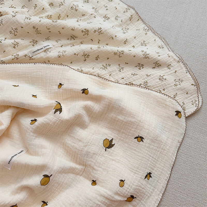 A reversible muslin cotton blanket with pillow set, featuring a lemon pattern on one side and a different small floral design on the other
