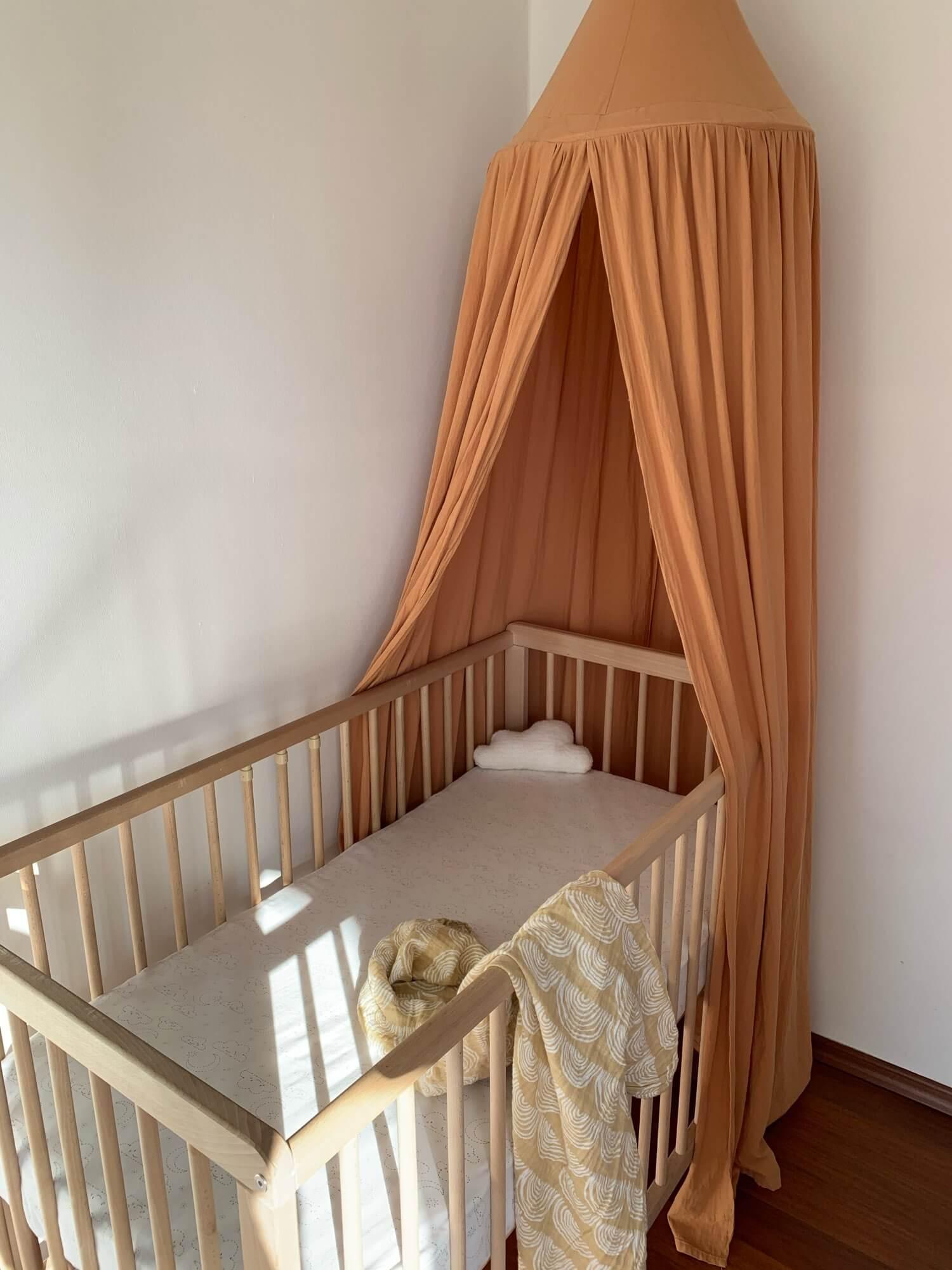 Caramel-colored nursery bed canopy mounted over a wooden baby crib.