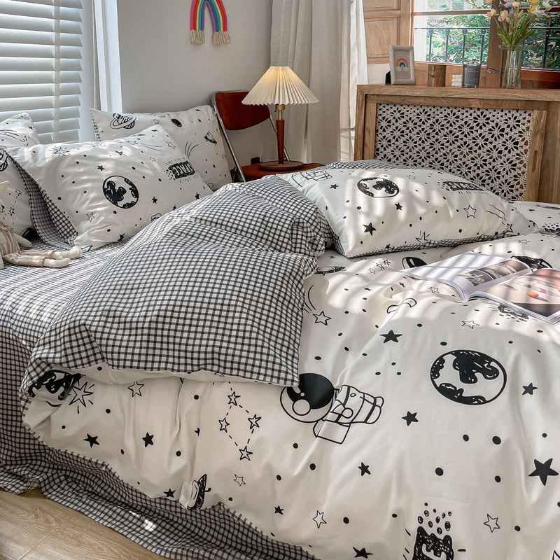 A close-up of the outer space kids' cotton bedding, showing a reversible design with one side featuring black and white planet illustrations and the other a subtle check pattern
