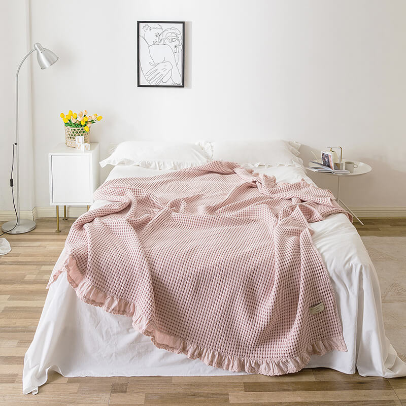 Pink cotton waffle blanket with ruffle edge displayed on a bed