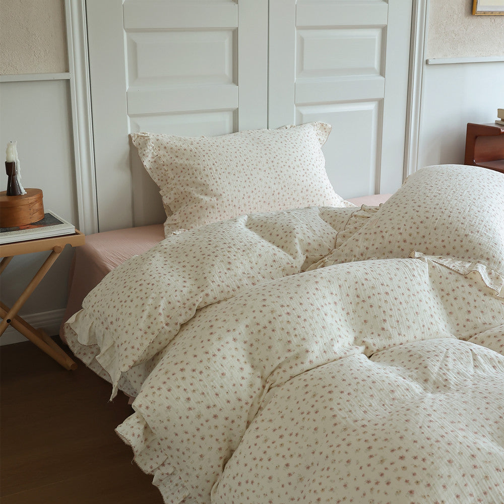 Ruffled floral comforter and pillow beside pink cotton flat sheet