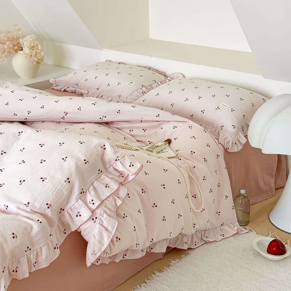 A full view of the pink cherry print ruffled duvet cover set on a bed in a bright room, showing the duvet, shams, and a solid pink flat sheet.