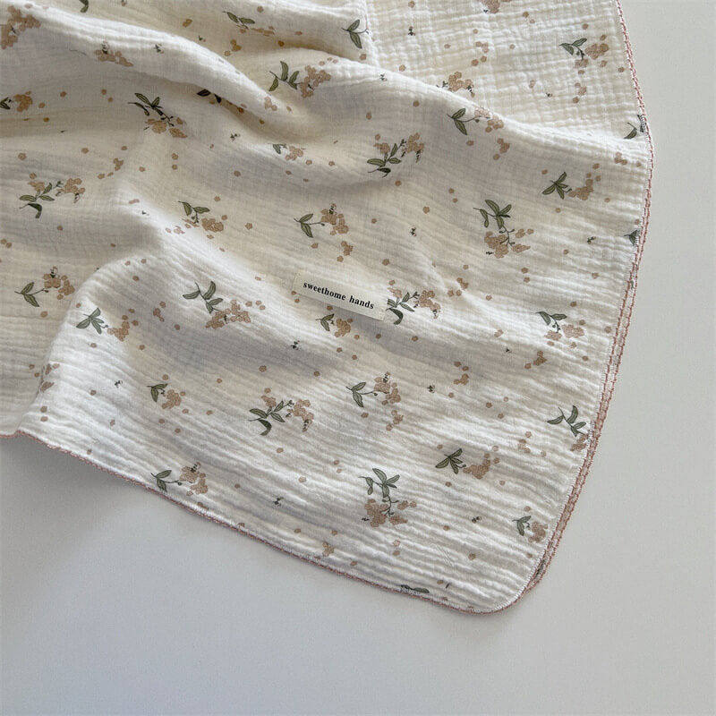 A white muslin baby blanket with a laurel floral print and a 'sweethome hands' tag.
