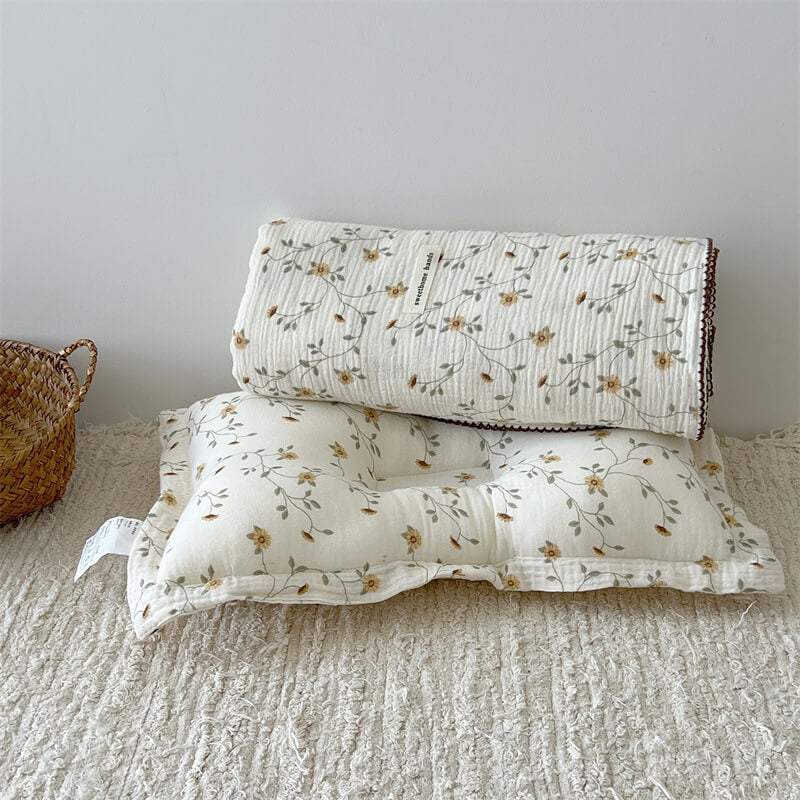 The yellow floral muslin receiving blanket and matching pillow set on a textured rug.