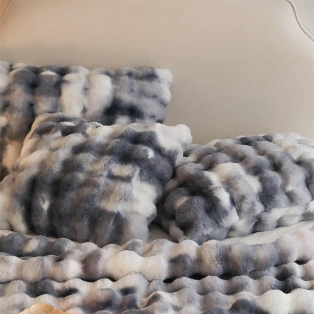 Close-up of a fluffy grey and white tie-dye patterned faux rabbit fur blanket and pillows.