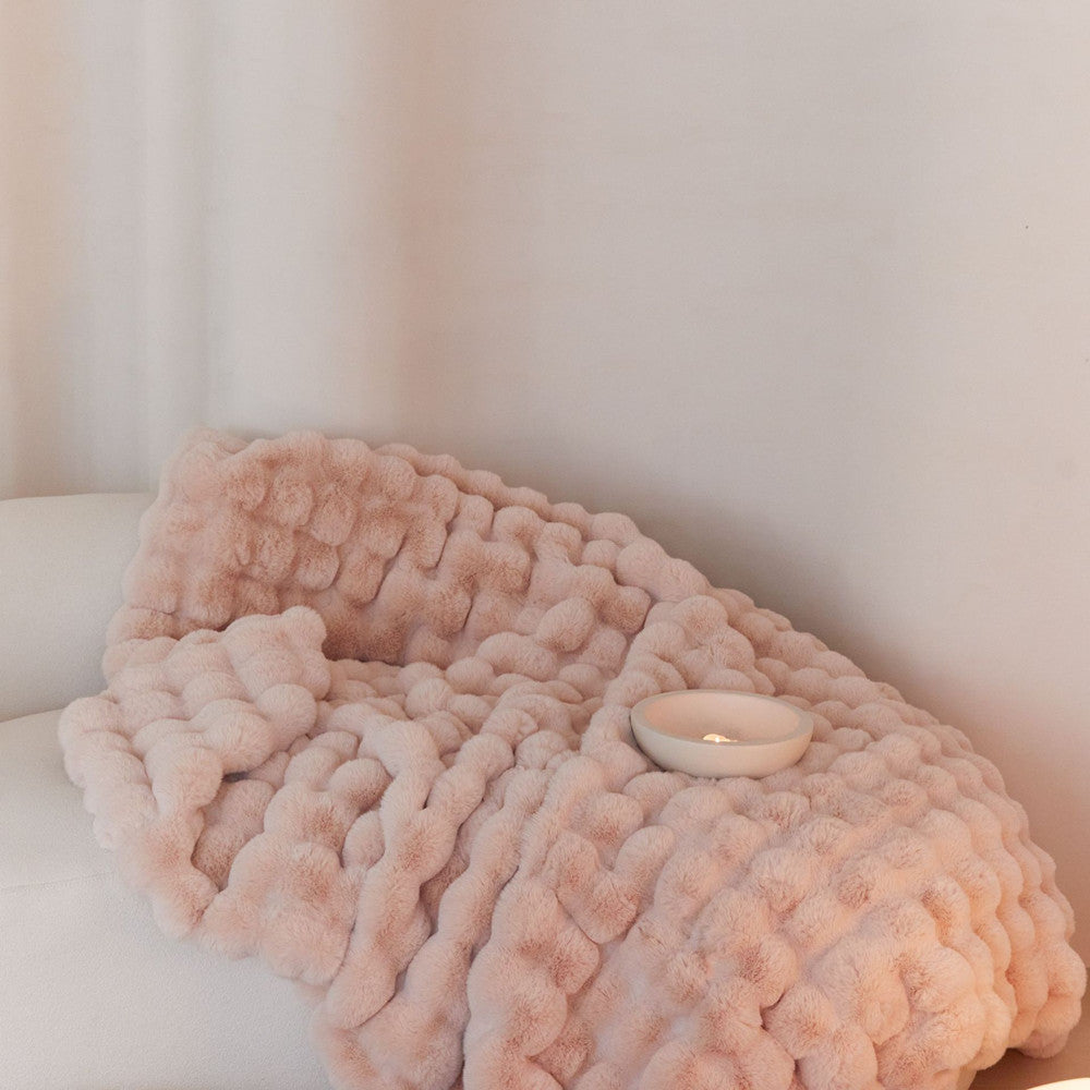 Close-up of a soft blush pink reversible faux rabbit fur blanket and a candle on a sofa