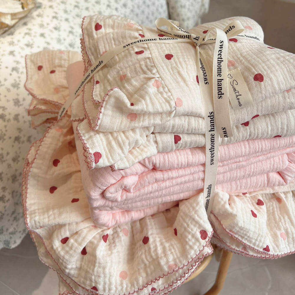 Stack of folded pink heart duvet cover set tied with a brand ribbon, highlighting the ruffled and crinkled cotton muslin