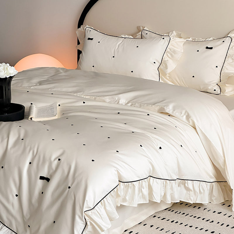 Side view of ivory bedding set with ruffled edges and bow detail