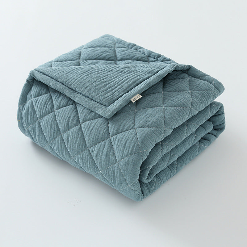 Folded sage green cotton muslin baby quilt with soft wrinkled texture on a white surface