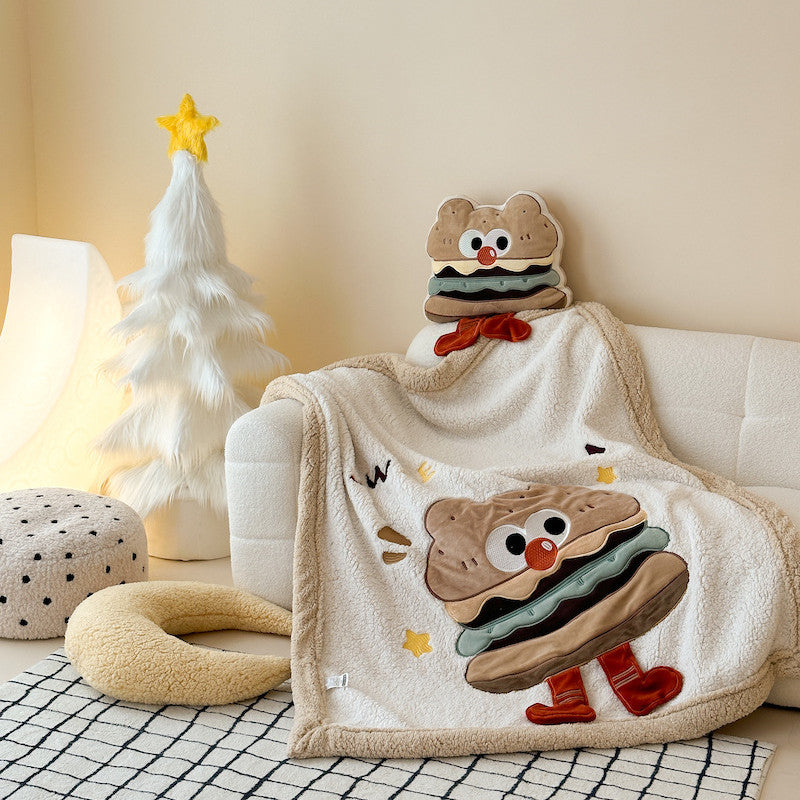 A plush sherpa baby blanket featuring a large hamburger character, styled on a white sofa with pillows.