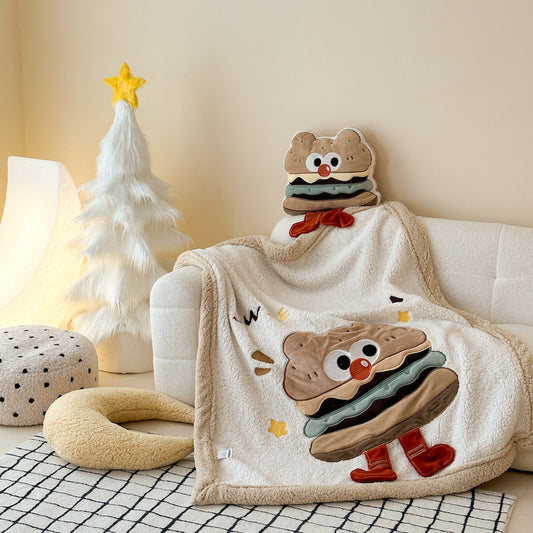 A plush sherpa baby blanket featuring a large hamburger character, styled on a white sofa with pillows.