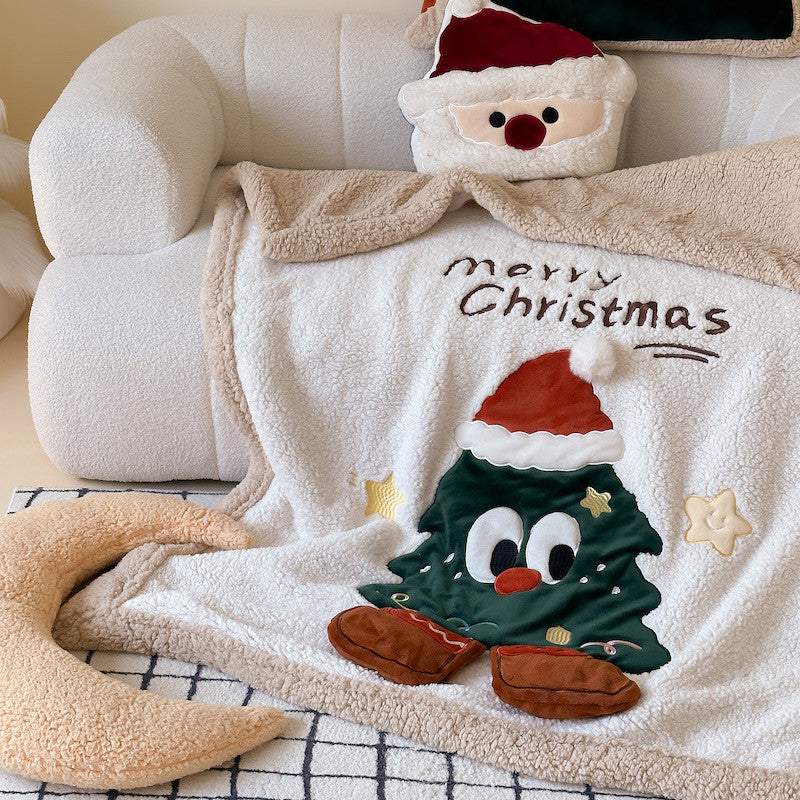 A detailed view of a reversible Christmas sherpa fleece blanket, showing the plush texture and an embroidered Christmas tree character.