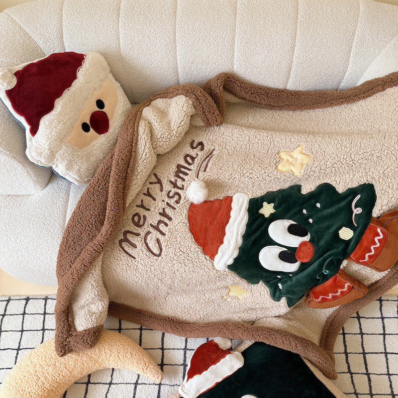 Overhead view of a reversible sherpa throw blanket with an embroidered Christmas tree character and a Santa-shaped pillow.