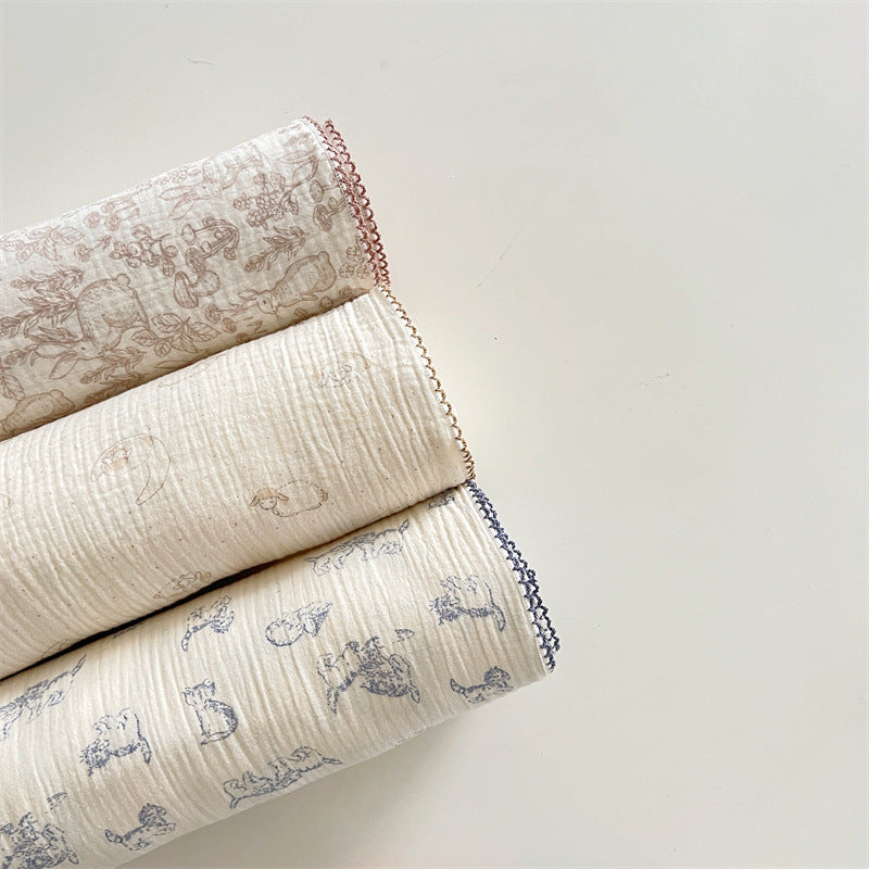 Three soft muslin baby blankets in woodland, lamb, and kitty patterns, rolled up side by side