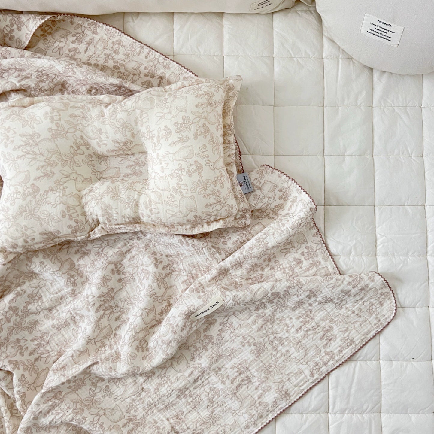 Woodland bunny print muslin blanket and pillow on a white quilted bed