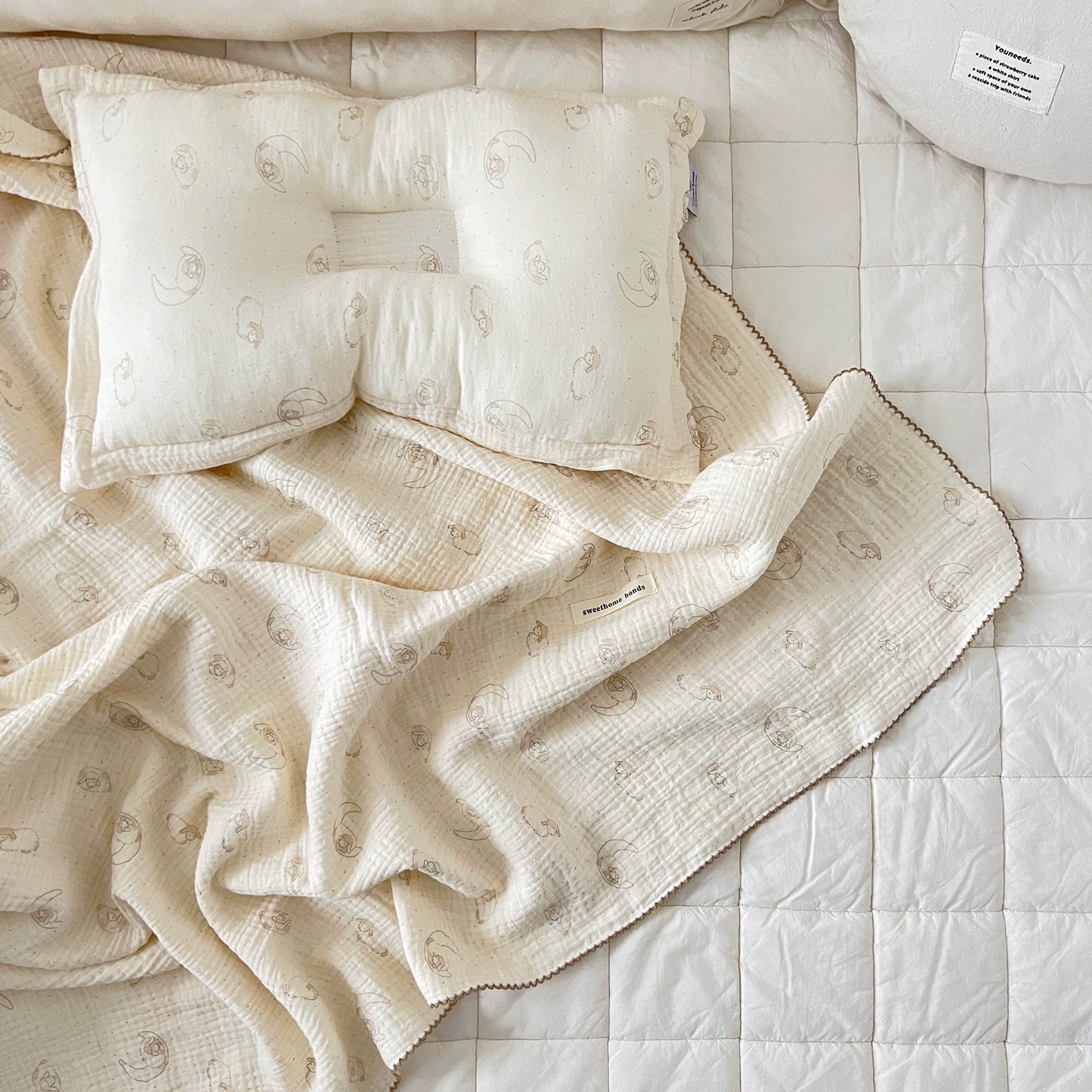 Lamb print muslin blanket with matching pillow, styled on a soft baby bed