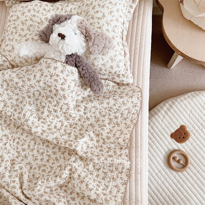 camellia floral muslin baby blanket and pillow set with a doll and toys on a bed.