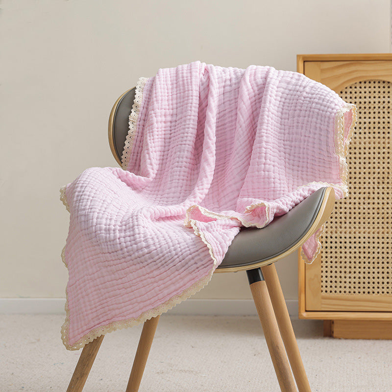 A light pink 6-layer muslin swaddle blanket with a decorative lace trim draped elegantly over a chair.