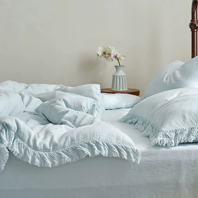 A stylish shot of a light blue cotton gauze duvet cover and pillows with decorative fringe, creating a fresh and tranquil bedroom atmosphere.
