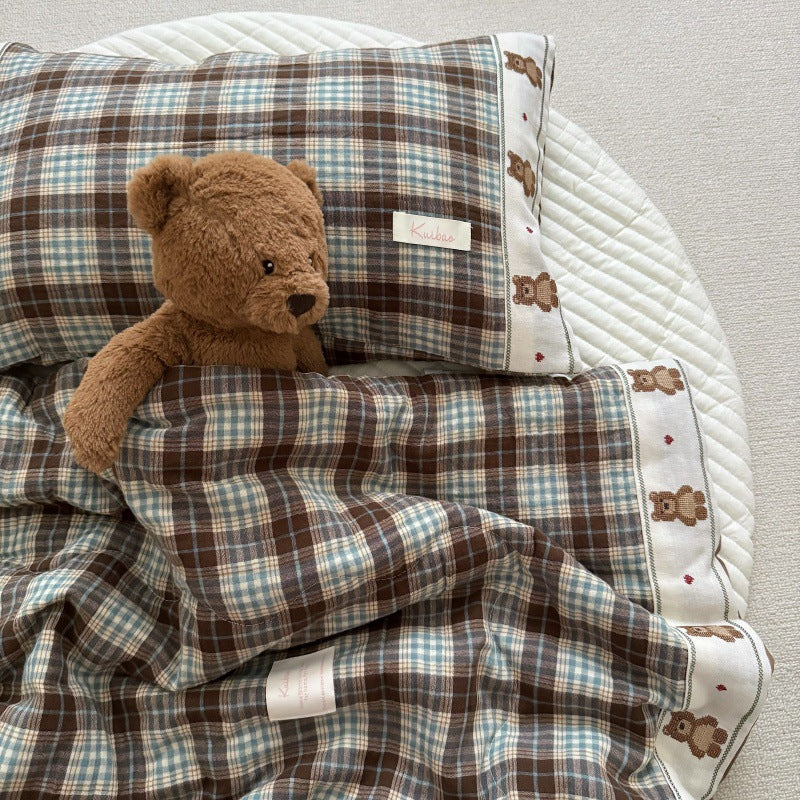Soft cotton gauze comforter with plaid pattern and teddy bear trim laid flat with matching pillow