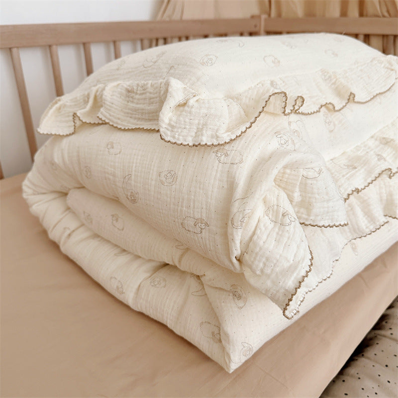 Cream cotton muslin lamb ruffle duvet cover set folded on a crib bed