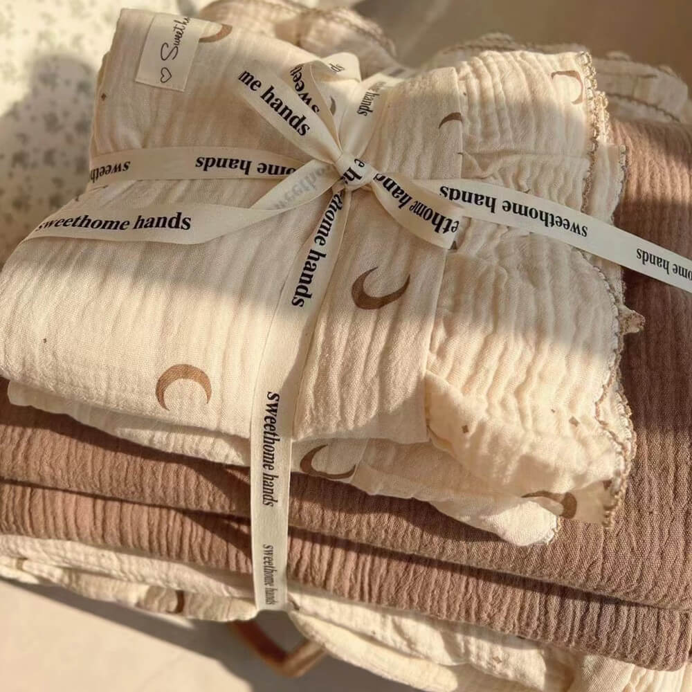A stack of folded moon and star print cotton muslin bedding with ruffled edges.