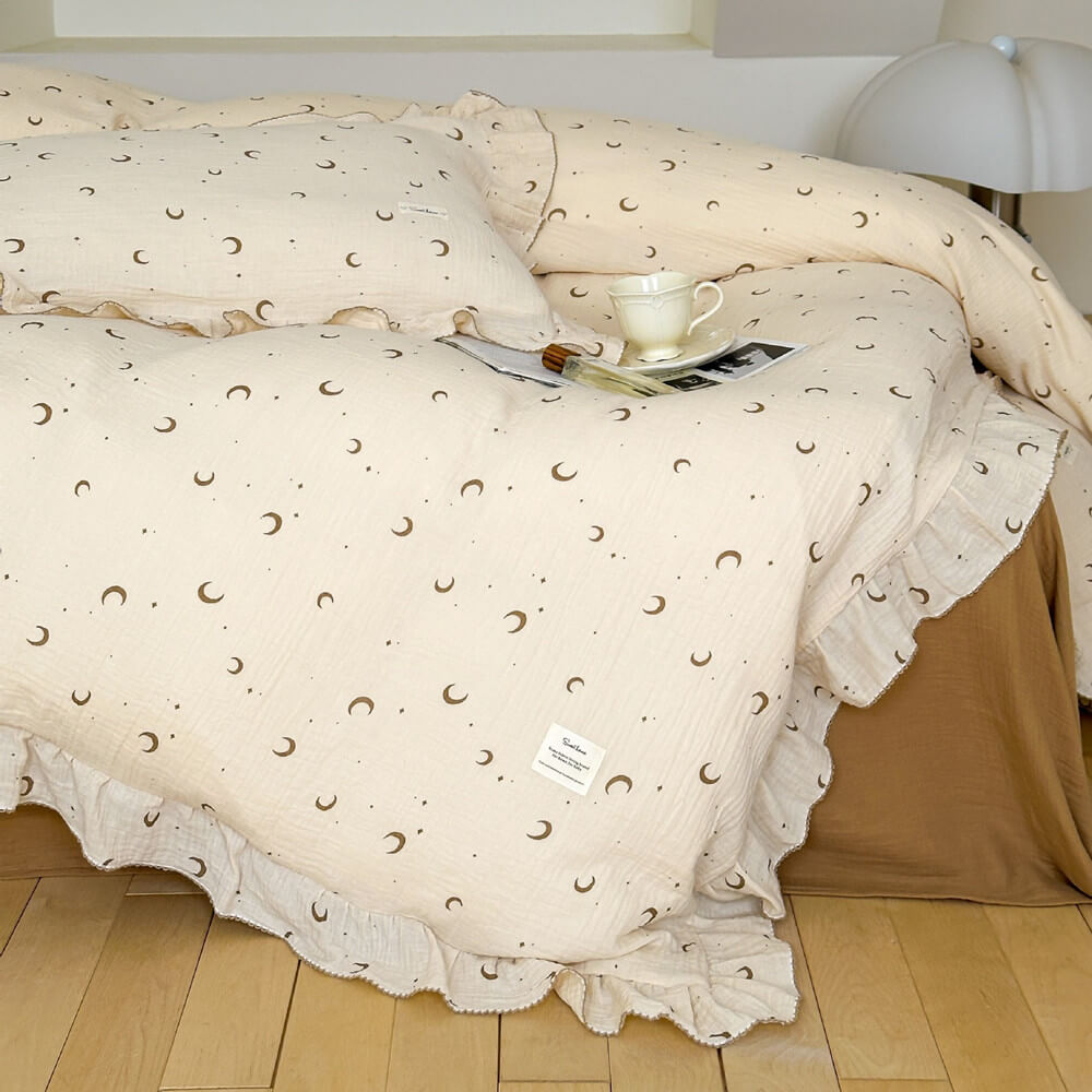 A bed styled with the moon and star print cotton muslin bedding and ruffled edges, with a teacup and book