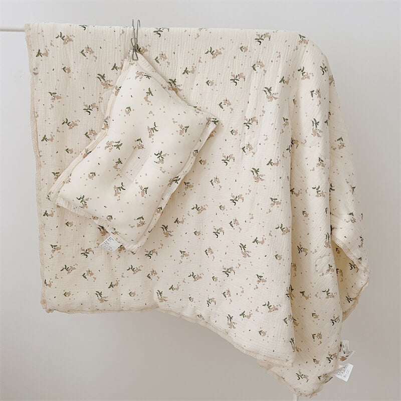 Cream floral cotton muslin baby blanket and matching pillow hanging on a hook