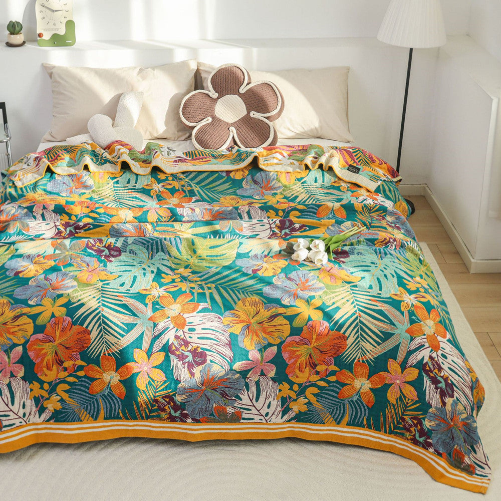 A front view of a bed covered with a colorful tropical paradise throw blanket featuring a mix of orange flowers and green leaves, with matching decorative pillows.